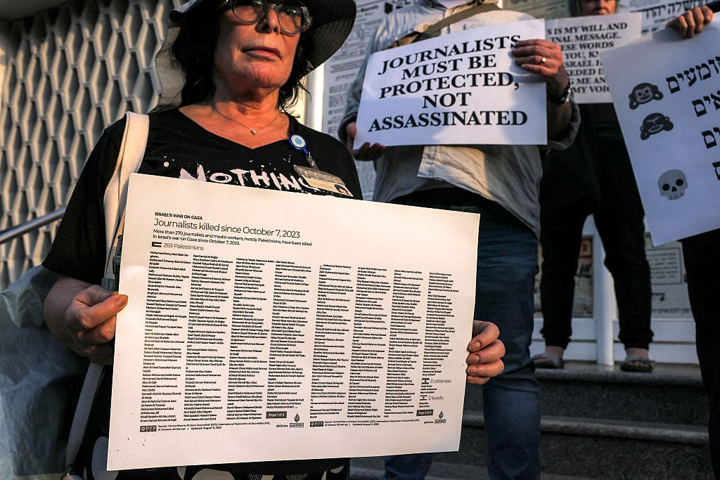 A woman holds a sign showing the names of journalists killed in Palestine, Lebanon, and Israel since October 7, 2023, during a protest in solidarity with journalists in the Gaza Strip and condemning the killing of Al Jazeera journalists days earlier, organized by Israeli and international journalists outside the Press House in Tel Aviv, on August 13, 2025. AHMAD GHARABLI/ AFP via Getty Images