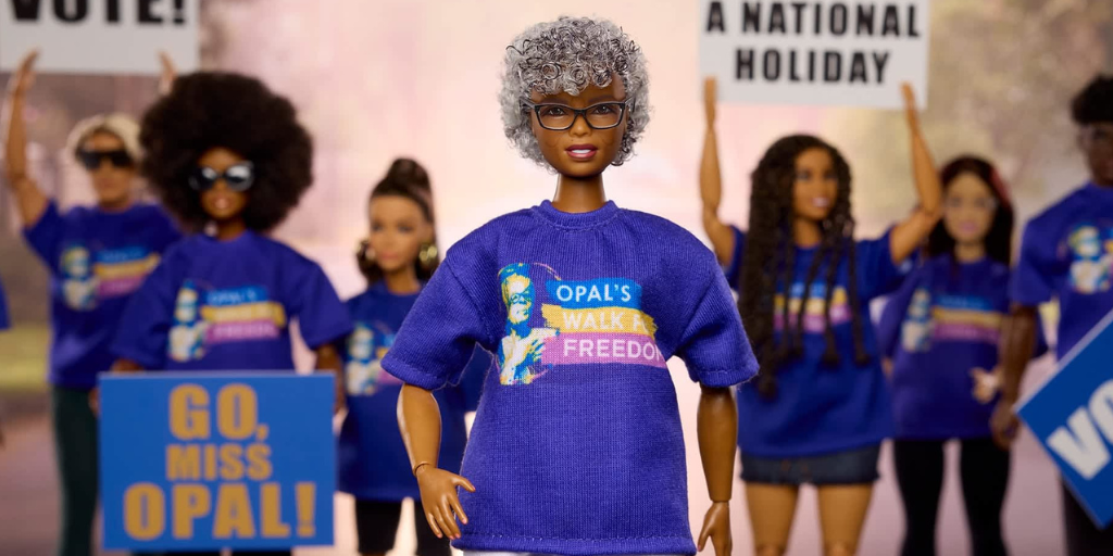 The Dr, Opal Lee Barbie wears a purple "Opal's Walk for Freedom" shirt and stands in front of a cheering crowd of Barbies.